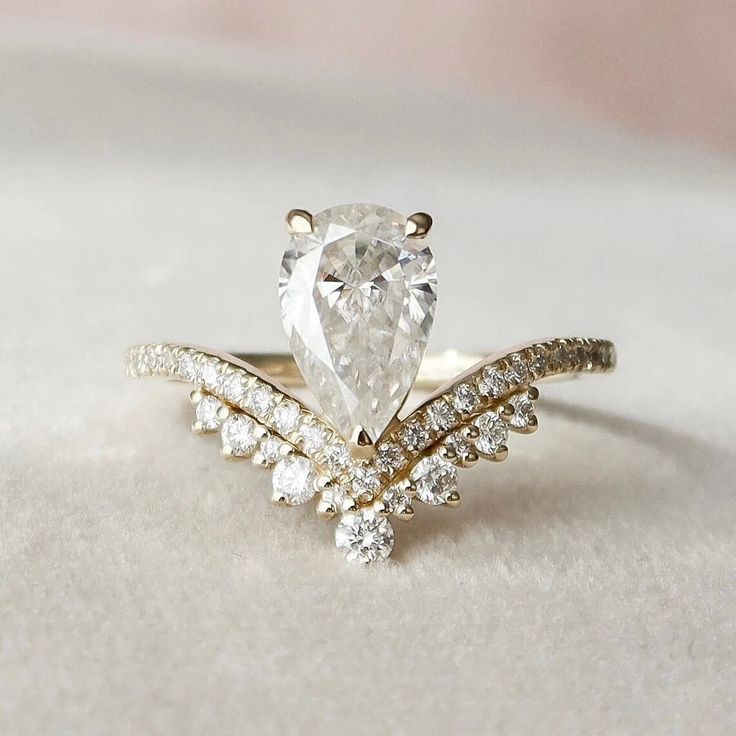 a pear shaped diamond engagement ring set on top of a white surface with diamonds around it