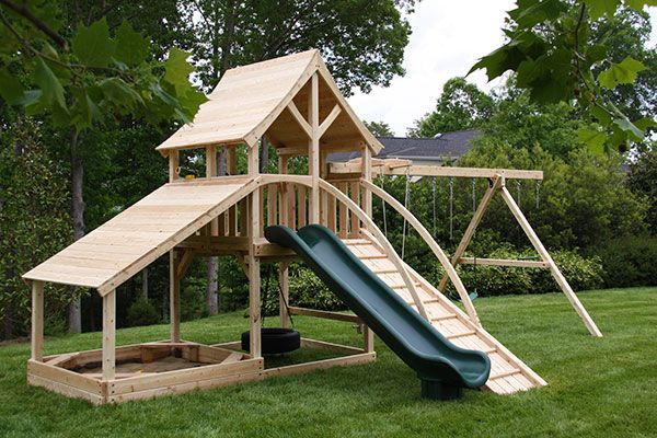 a wooden play set in the grass with a slide and climbing frame attached to it