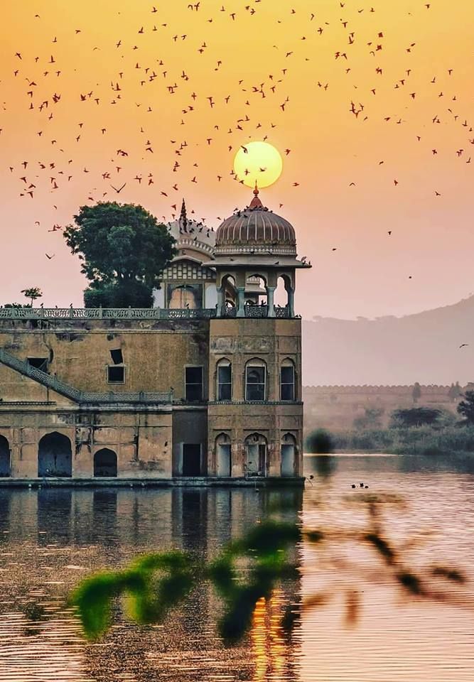 the sun is setting over an old building with birds flying around it and in the sky