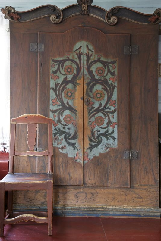 an old wooden chair sitting in front of a large door with floral designs on it