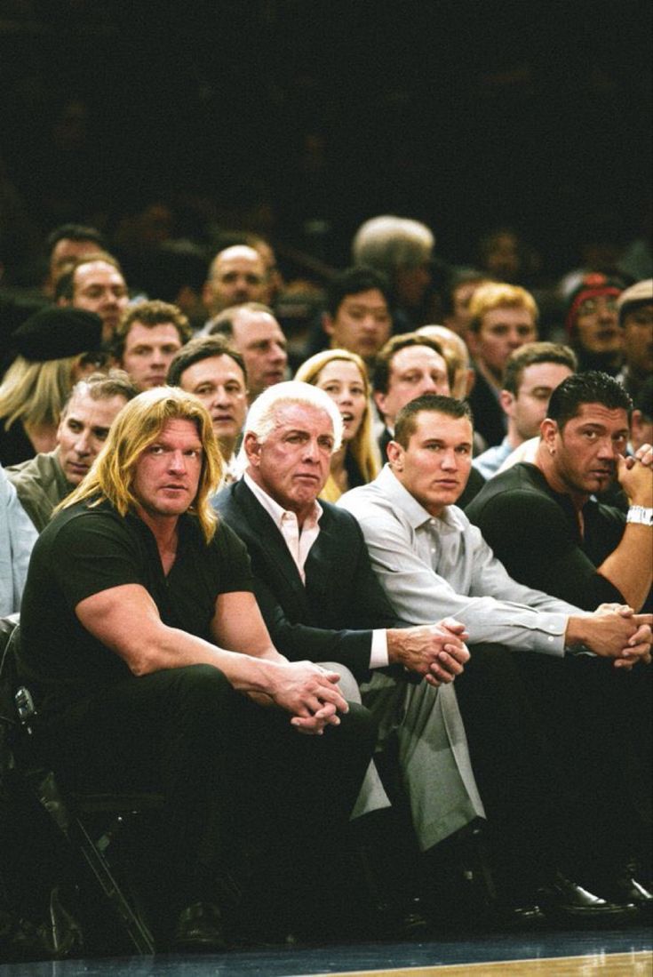 two men sitting next to each other in front of a crowd at a basketball game