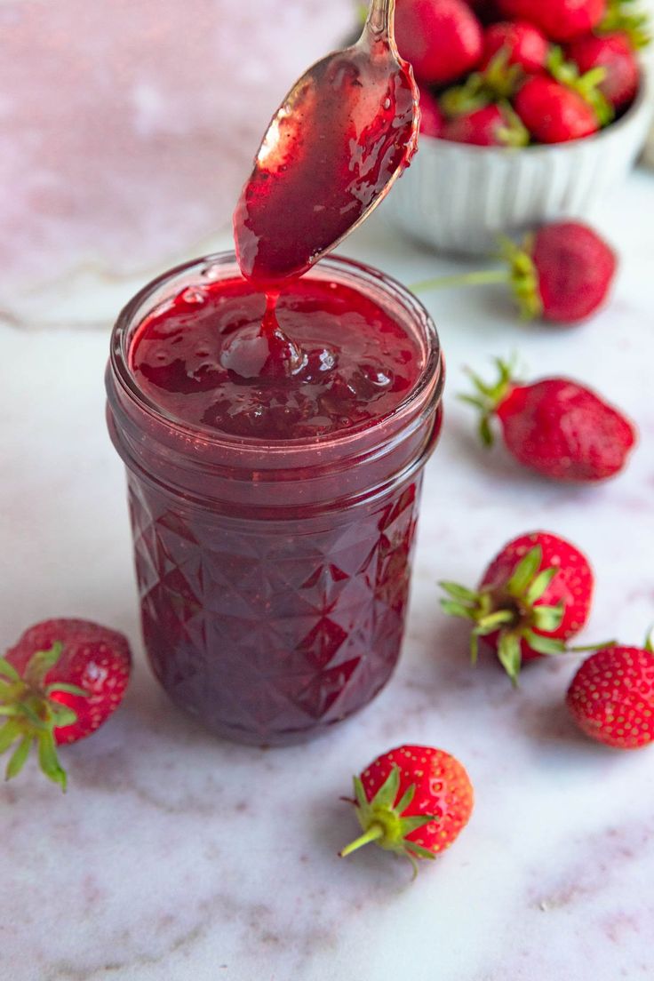 a spoon full of jam with strawberries in the background