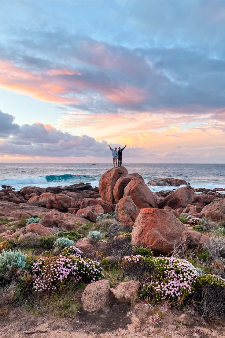 two people standing on top of a rock near the ocean with their arms in the air