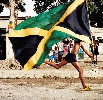 a woman running with a jamaica flag on her back while people watch from the sidelines