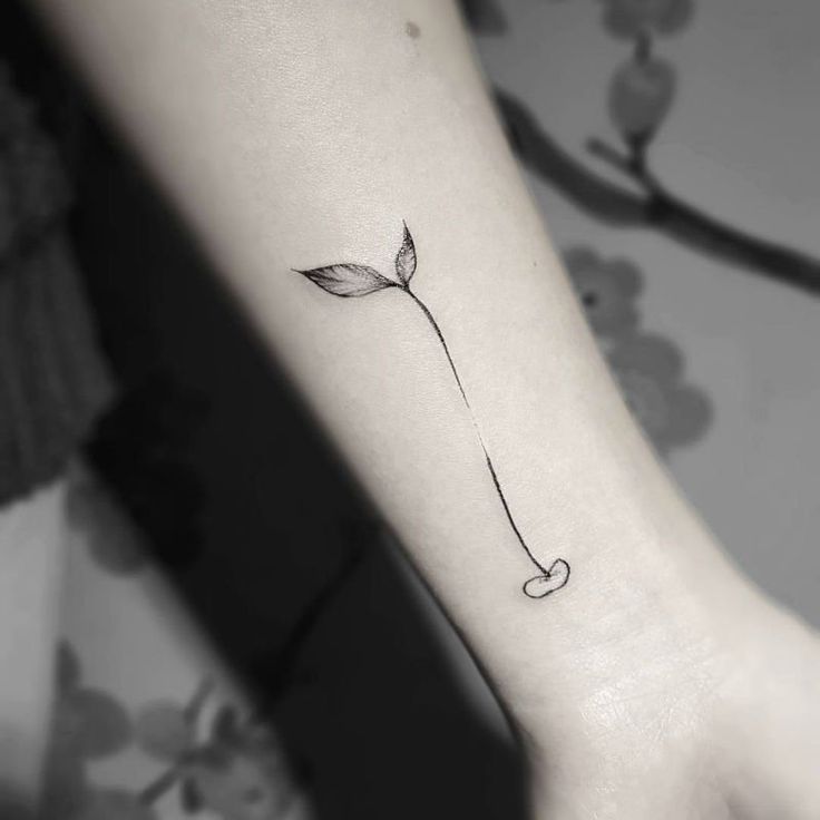 a single flower tattoo on the left inner forearm and wrist, with an arrow in the middle