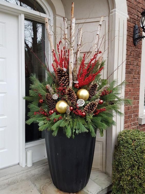 a potted plant with pine cones, berries and other decorations on the front porch