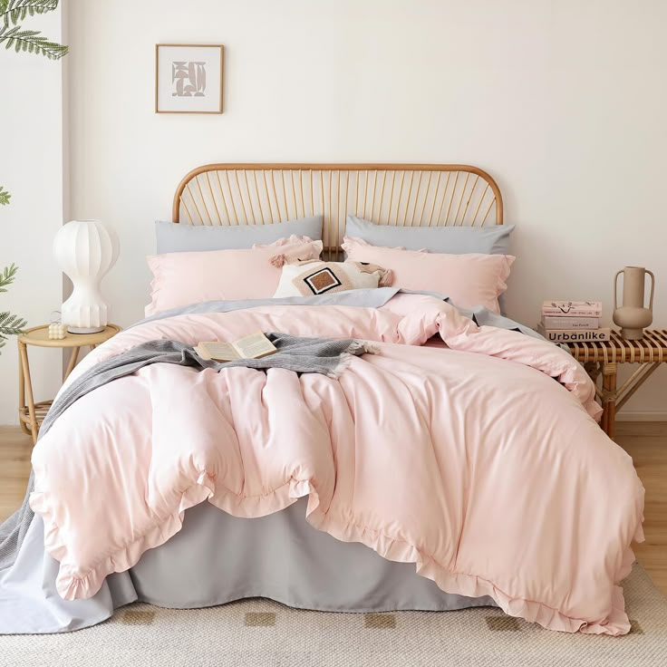 a bed with pink and grey comforters in a white room next to a wooden headboard