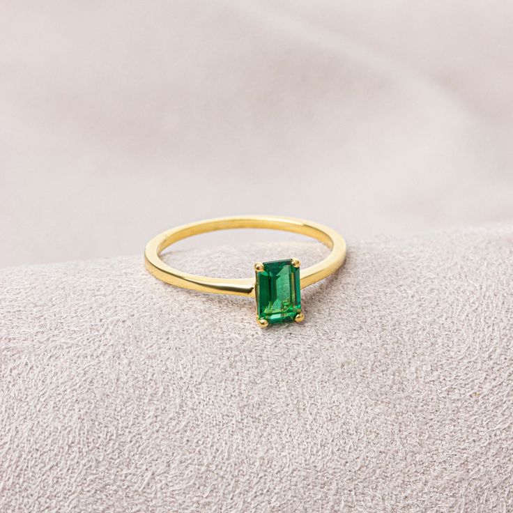 a gold ring with an emerald colored stone in the center on a white surface,