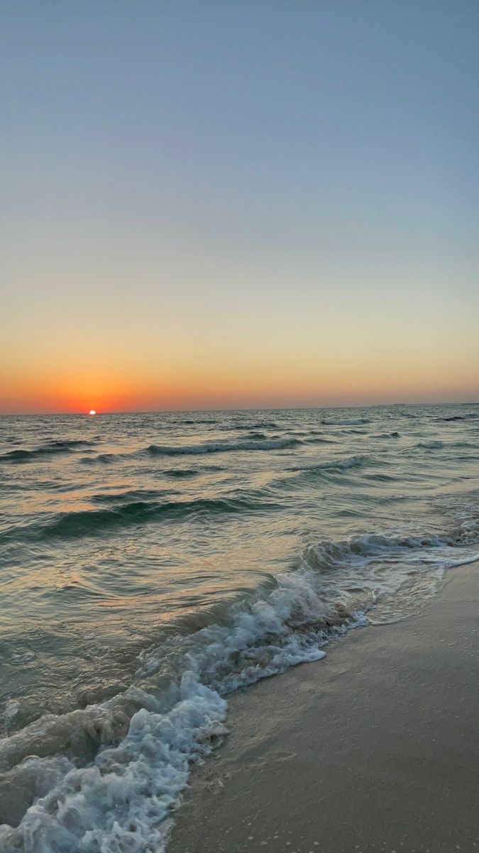 the sun is setting over the water at the beach with waves coming in to shore