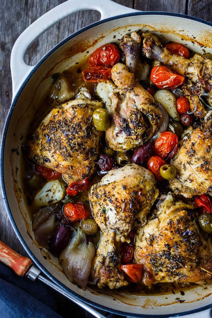 a pan filled with chicken and vegetables on top of a wooden table