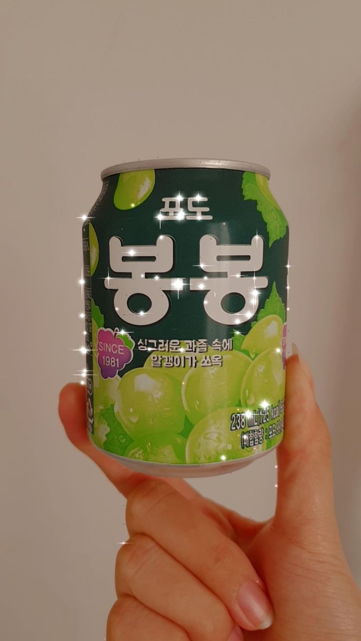 a person holding up a can of soda with grapes on the top and green leaves on the bottom