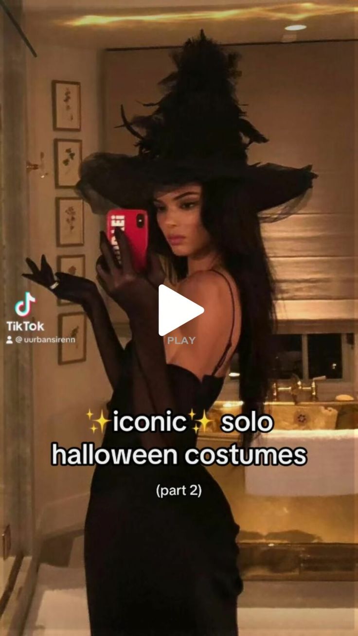 a woman in a black dress and hat holding a cell phone while wearing a witches costume