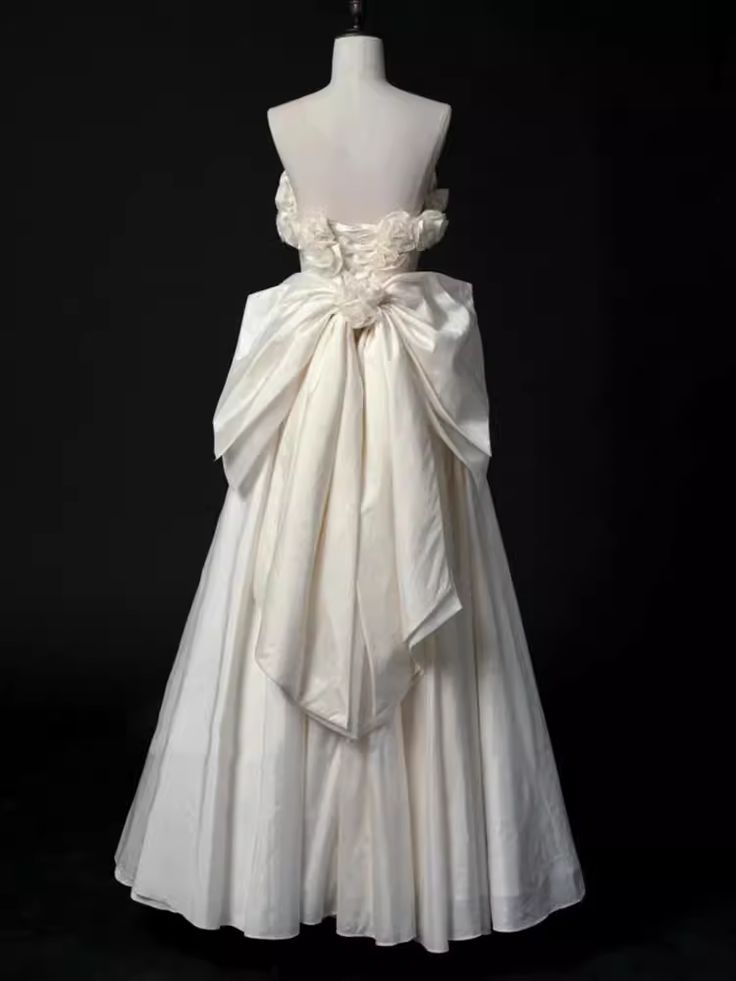 a white wedding dress with a large bow on the waist and back, sitting on a mannequin