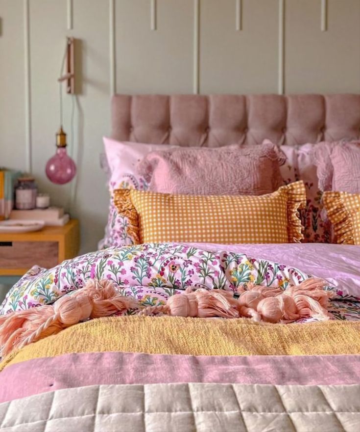 a bed with pink and yellow sheets, pillows and blankets on it's headboard