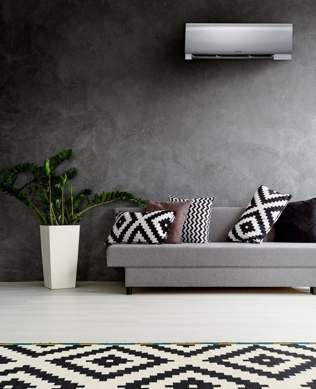 a living room with a couch, rug and air conditioner on the wall behind it