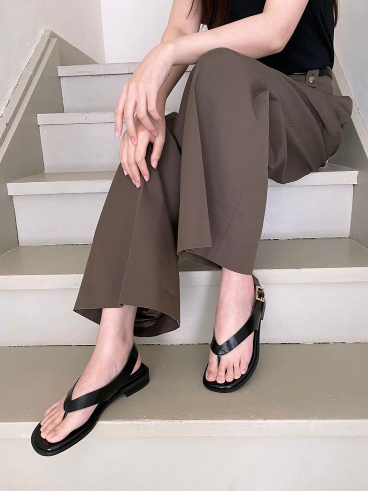 a woman is sitting on the steps wearing brown pants and black sandals with her legs crossed