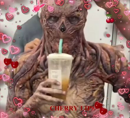 a man in an alien costume holding a drink and looking at his cell phone with the caption cherry lip