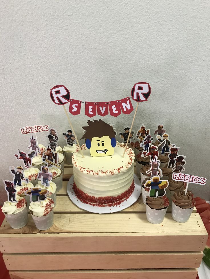 a birthday cake and cupcakes on a wooden table with red ribbon banner in the background