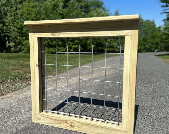 a wooden frame with a metal grid in the middle on a paved road next to some trees