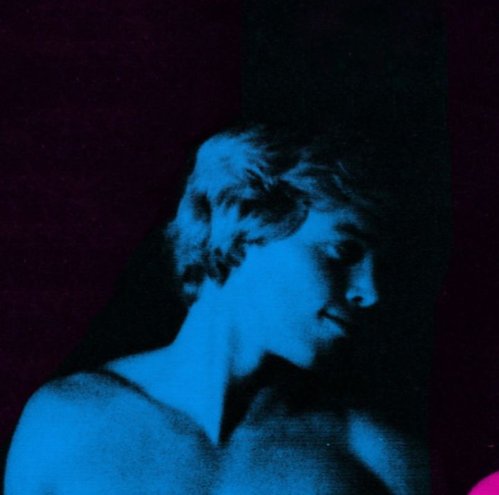 a man with no shirt on standing in front of a blue and pink wall next to another man