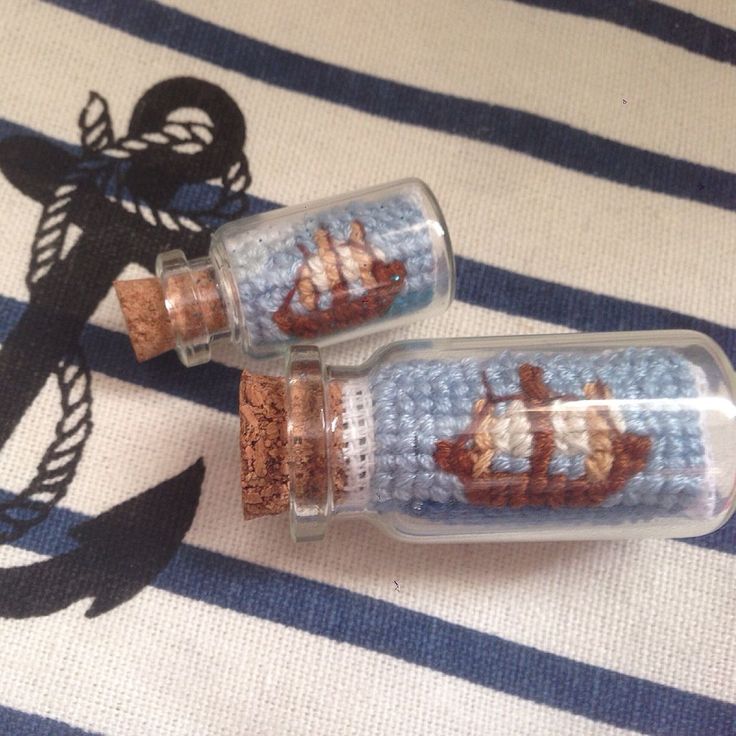 two glass bottles with ships in them sitting on a striped cloth