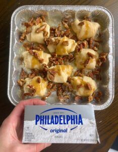 a person holding up a box of food with cheese and nuts on it, next to a package of philadelphia crackers