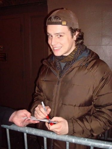 a man standing in front of a metal fence holding a pen and writing on paper