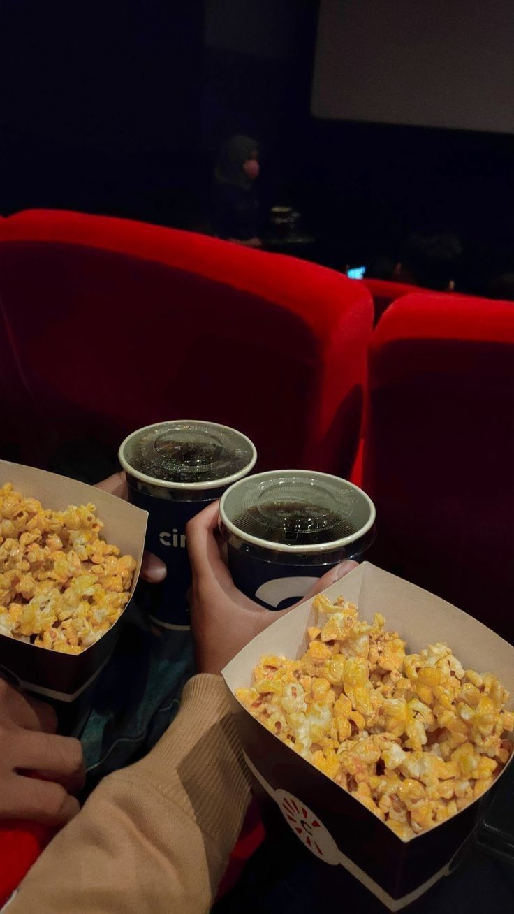 two people holding up boxes of food in front of red chairs at a movie theater