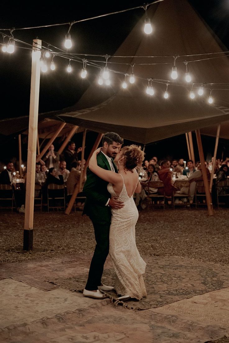 a bride and groom sharing their first dance under the tent at night with string lights