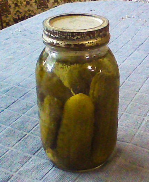 a jar filled with pickles sitting on top of a blue tablecloth covered table