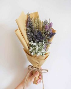 a person holding a bunch of flowers wrapped in brown paper