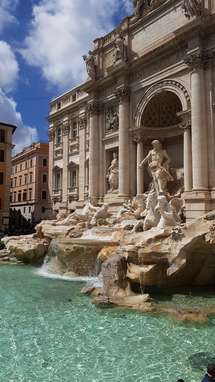 people are swimming in the water near some statues and buildings with columns on either side