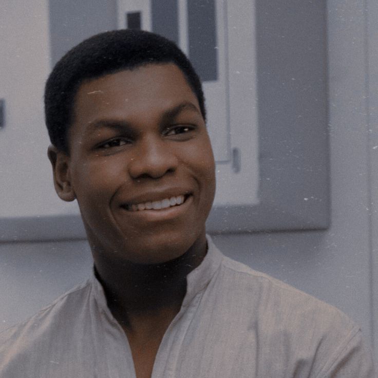 a young man smiling in front of a white wall with a clock on it's side