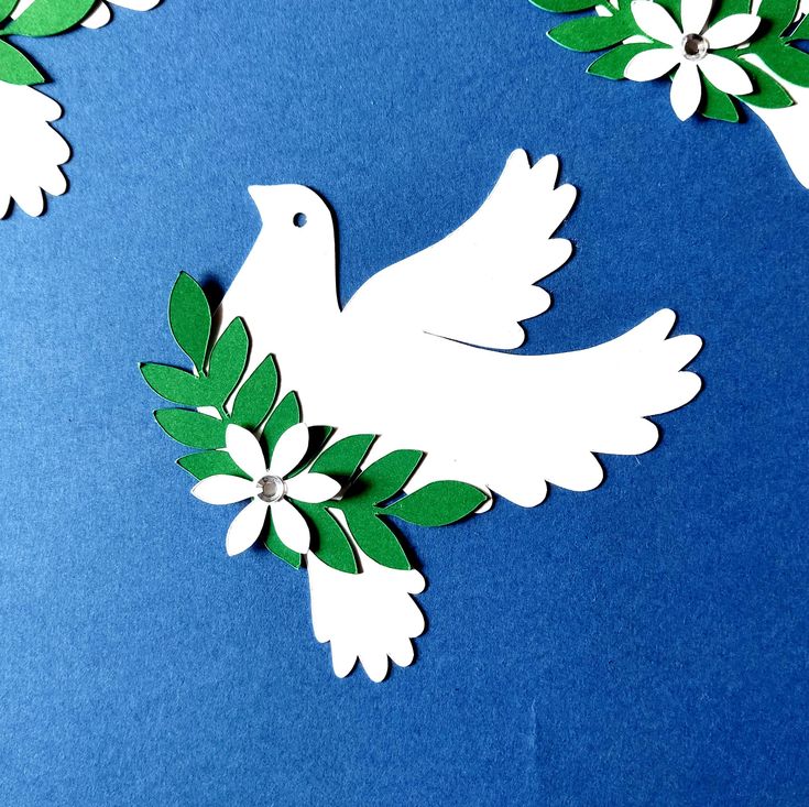 white paper dove with green leaves and flowers on blue background, cut out to look like an origami bird