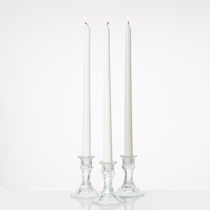 two white candles sitting next to each other in front of a white wall and floor