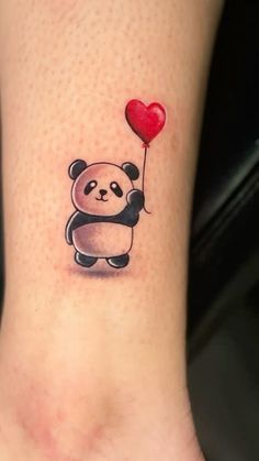 a small panda bear holding a red heart balloon tattoo on the ankle, with an air balloon attached to it's leg