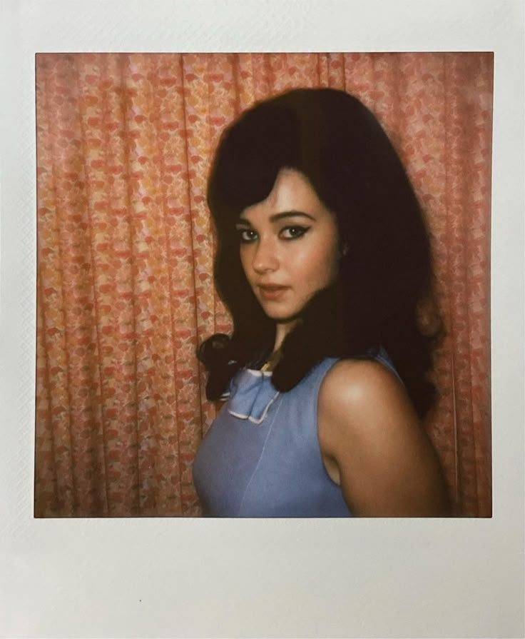 an old photo of a woman with long black hair and blue dress in front of a curtain