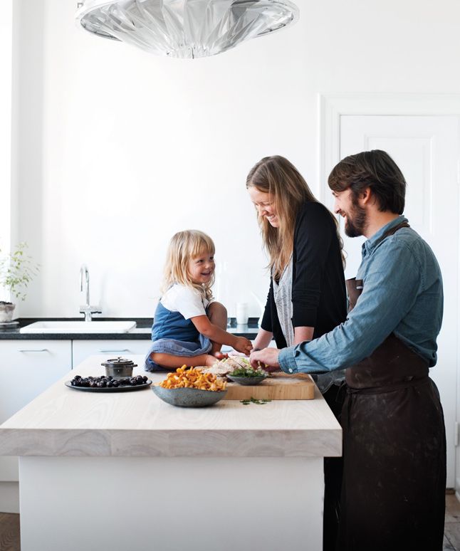 two adults and a child are preparing food on a kitchen counter top in front of a light fixture