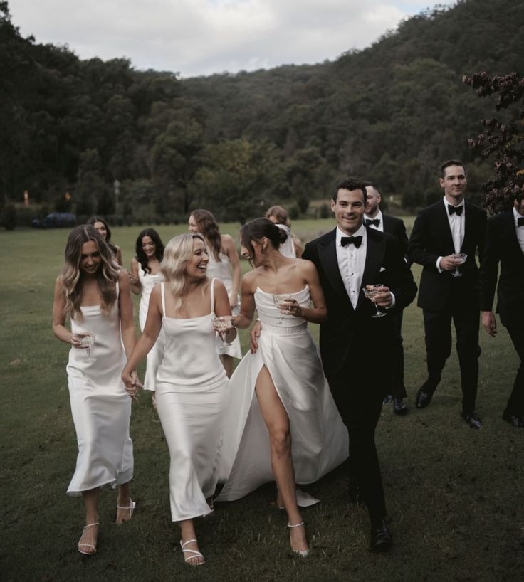 a group of people dressed in formal wear walking through the grass with one woman wearing a white dress