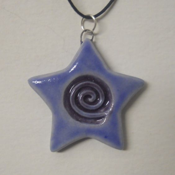 a blue and white ceramic star with a spiral design hanging from a leather cord necklace