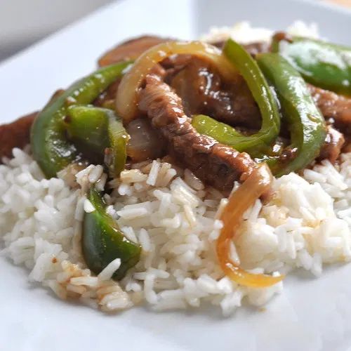 a white plate topped with rice and meat covered in sauce on top of green peppers