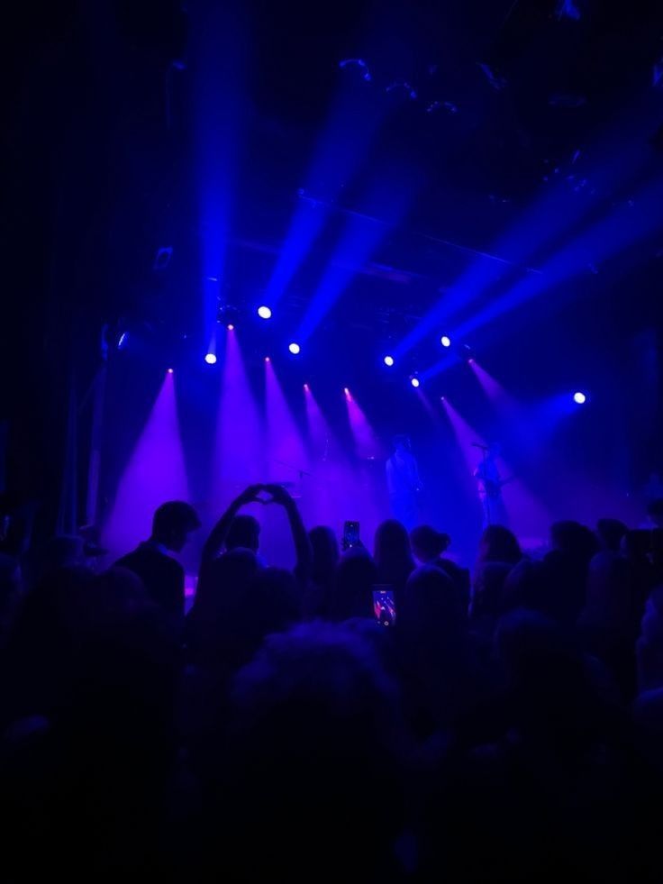 people are standing in front of purple and blue lights as they perform on the stage