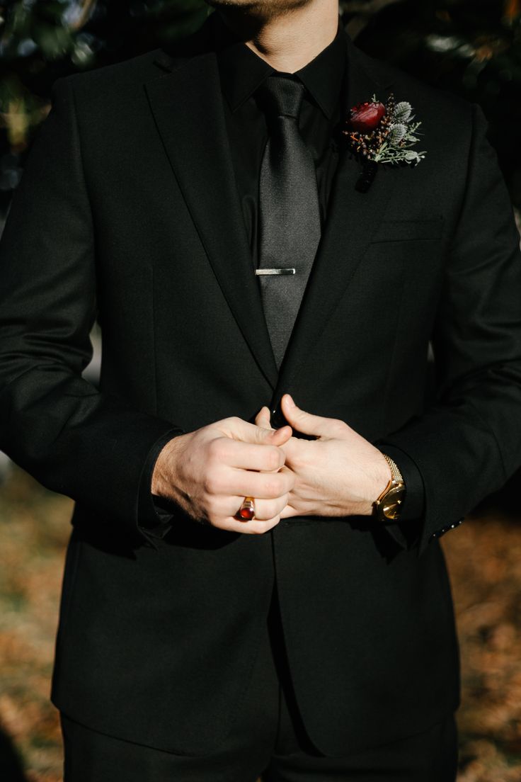 a man in a black suit and tie with his hands on his chest looking down