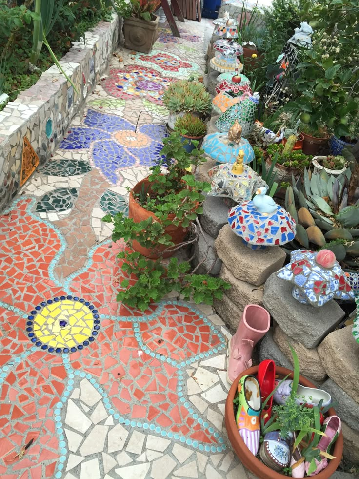 a garden filled with lots of potted plants next to a stone wall and walkway