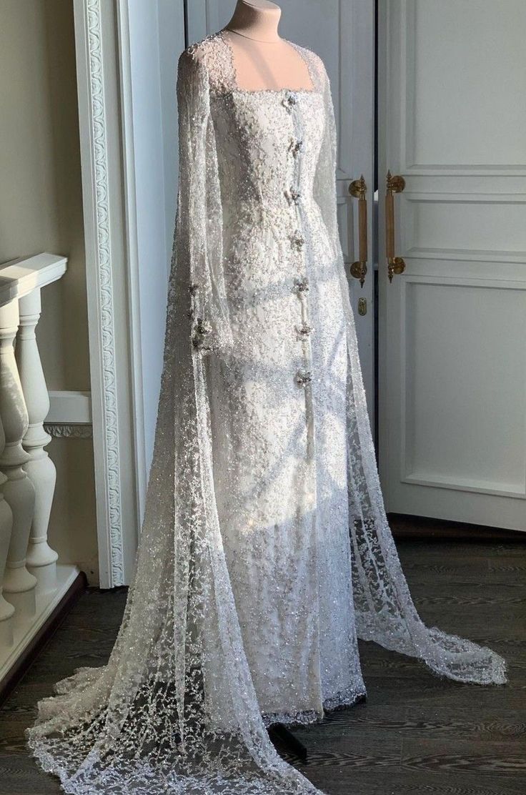 a white wedding gown on display in front of a door with an elaborate lace cape