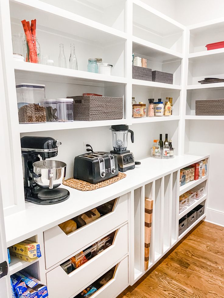 an organized pantry with white shelves and drawers