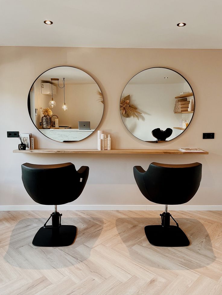 two round mirrors on the wall above black chairs