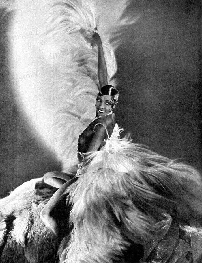 a black and white photo of a woman with feathers on her head sitting on a chair