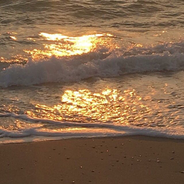 the sun is setting over the water at the beach with waves coming in to shore