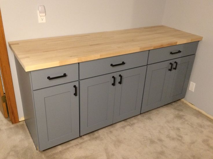 an empty room with gray cabinets and wood counter top in the middle, on carpeted floor